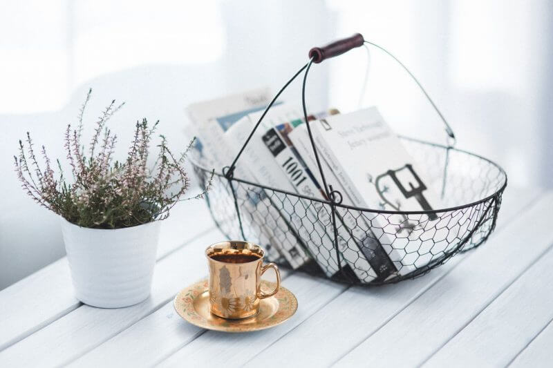 basket and coffee cup on a white table with plant.