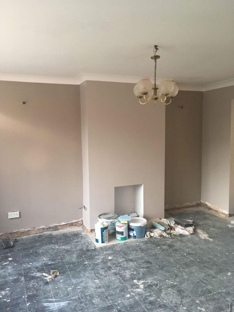 Empty living room with no carpets or skirting board. Fireplace in the centre back wall.