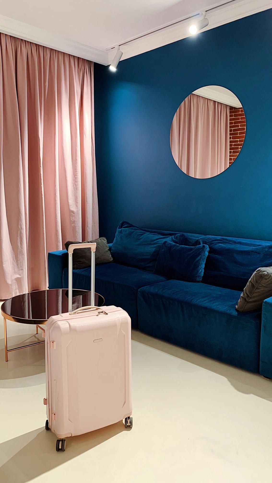 A hotel room with a dark blue feature wall next to some light pink voile curtains