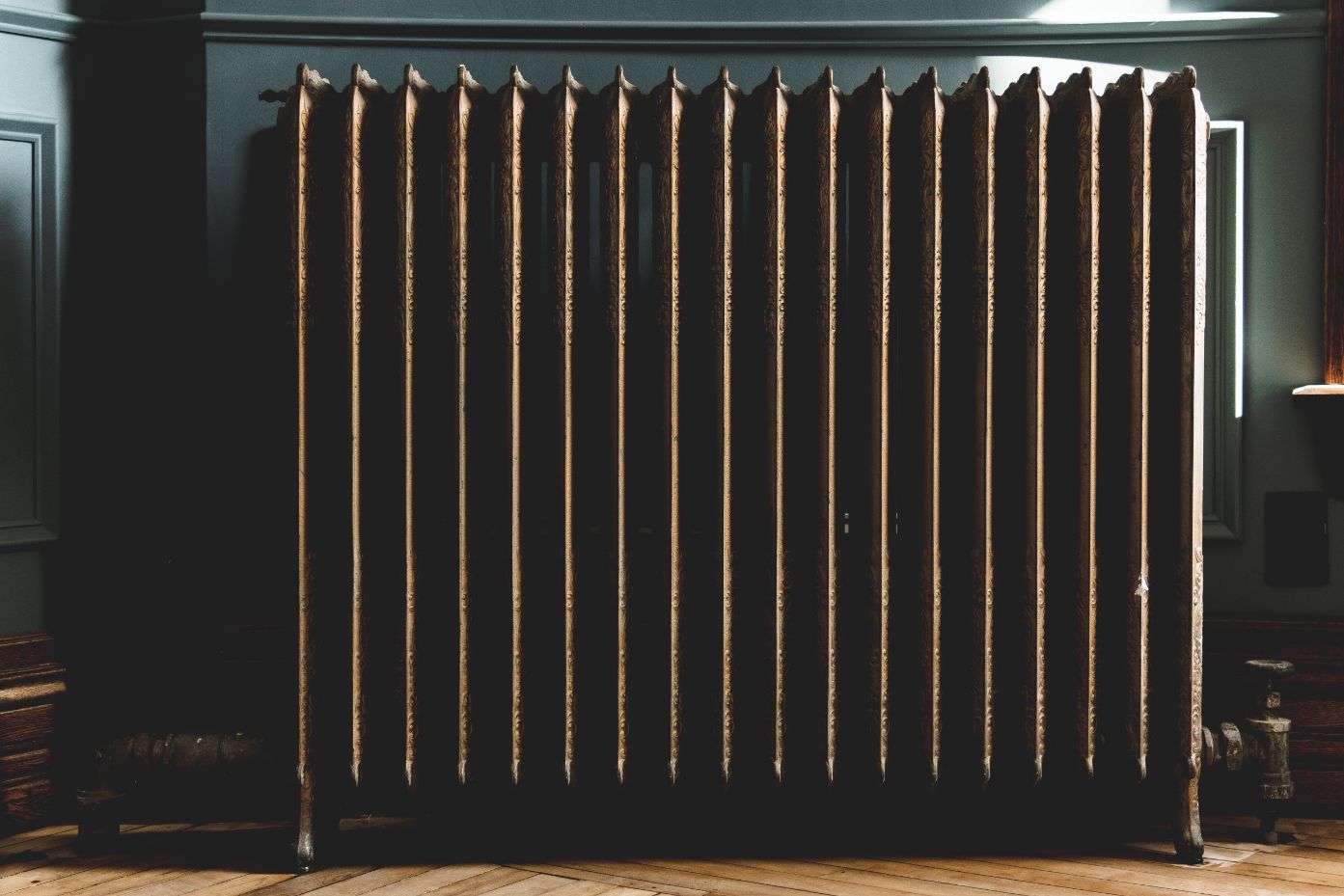 Cast Iron radiator in a bronze colour in a period home, against a wall of green panelling