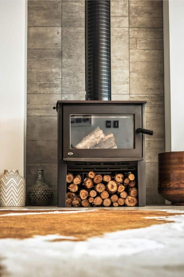 Wood burner against a brick chimney with logs stacked underneath