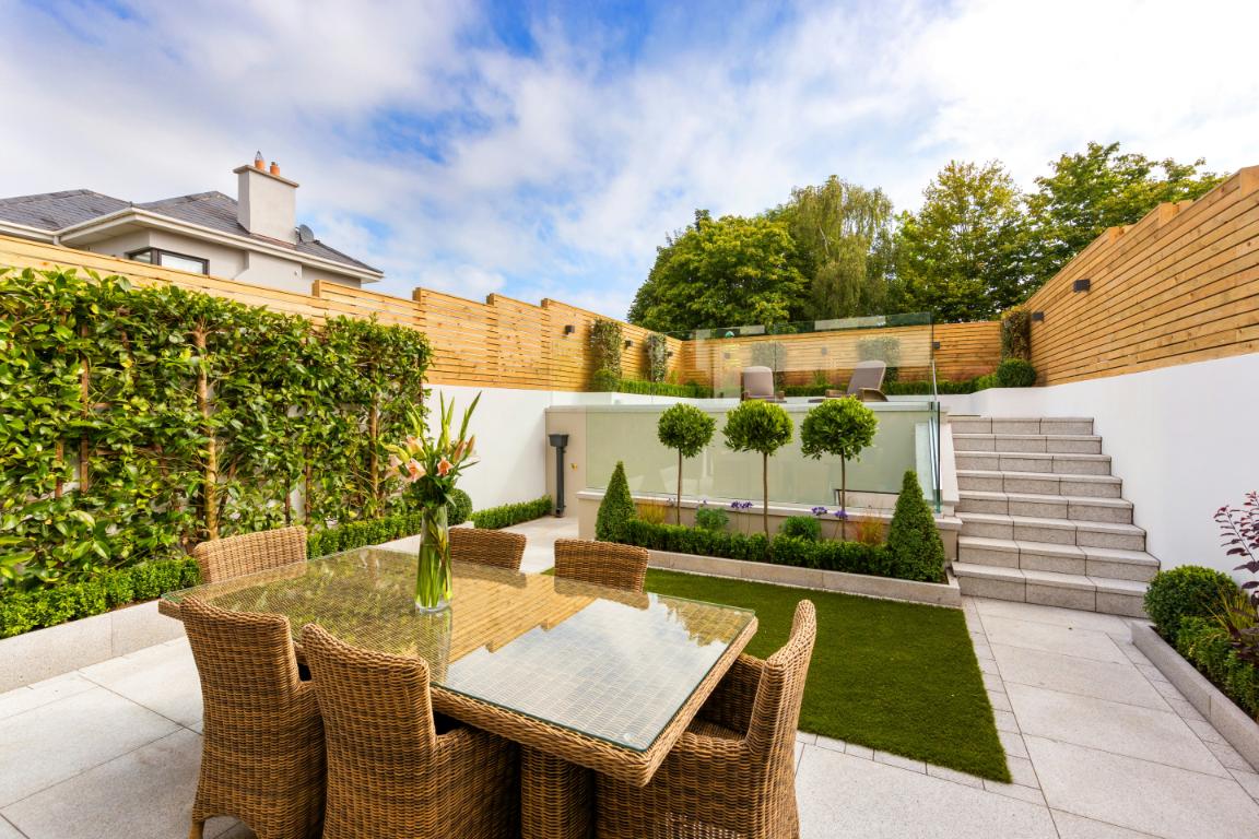 Rattan furniture in a modern garden with paving and circular box trees
