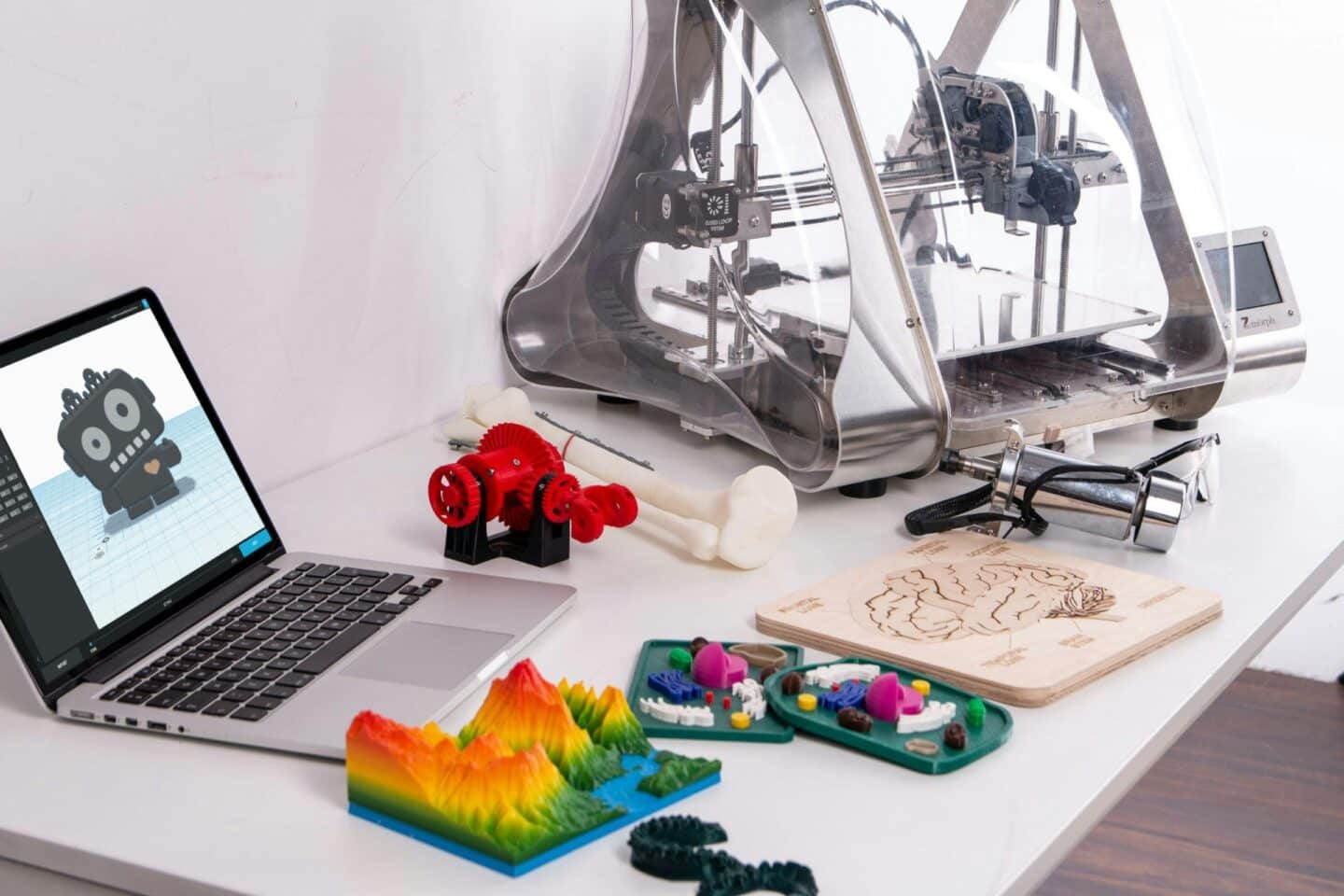 A 3D printer on a desk next to some printed out items