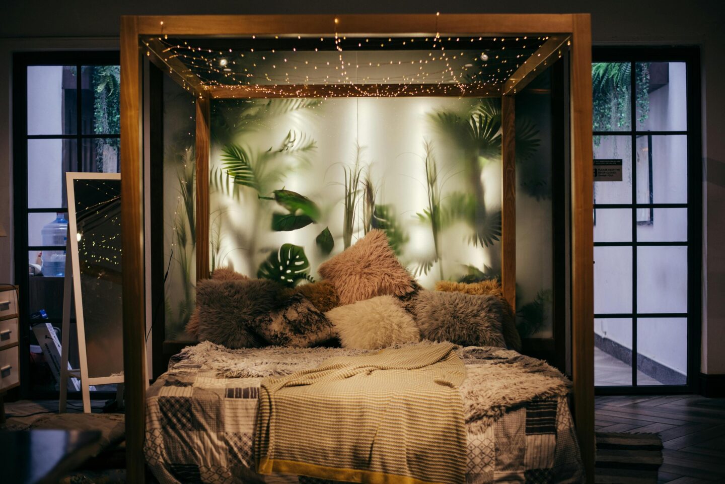 A bed with a plant backdrop and fairy lights on the ceiling