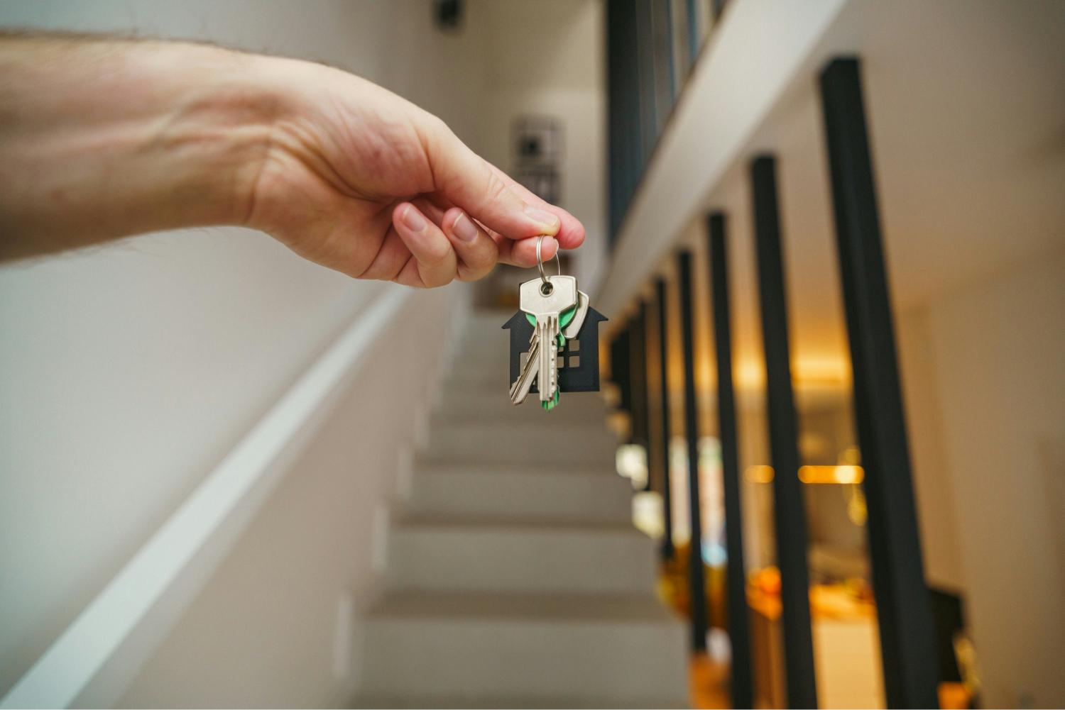 Someone holding up a set of house keys in front of a modern staircase