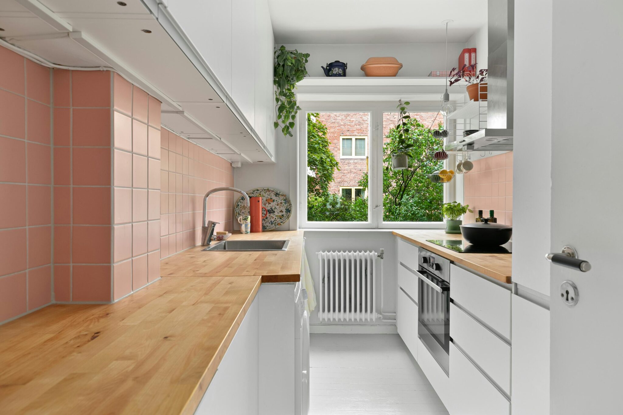 A white kitchen with wooden worktops and pink tiles on the walls