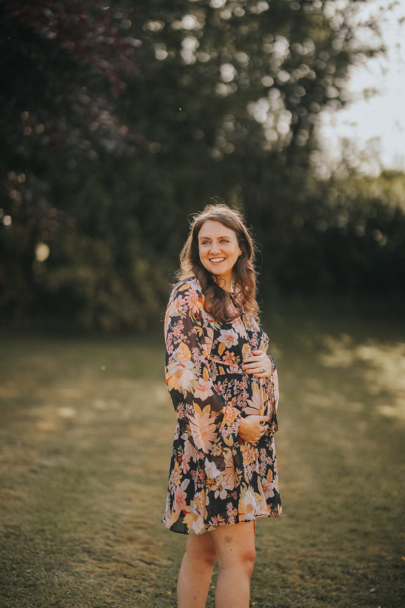 Sarah holding her baby bump in the countryside with the sun shining